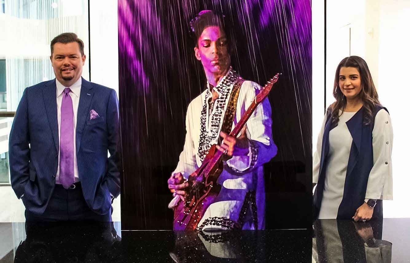 Attorneys Carlos Cortez and Megna Wadhwani standing next to a large photo of Prince, one of their favorite entertainers